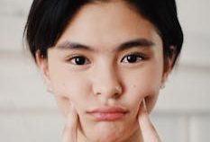 A close-up portrait of a young woman making a cute facial expression indoors.